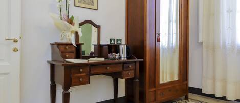 A wooden desk with drawers, a mirror, and a vase with flowers.