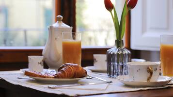 Una mesa de desayuno con cruasanes, tazas de café y un florero con tulipanes.