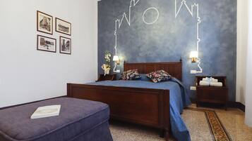 Ein Schlafzimmer mit einem hölzernen Bett, einem kleinen Nachttisch, Bildern in Rahmen an der Wand und einer blauen Wand mit geometrischem Muster.