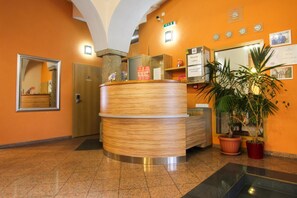 A reception desk with a wooden finish, a large mirror, and a potted plant. - Hotel Prajer (Vodňany)