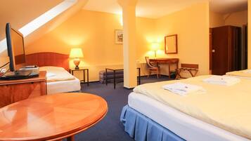 A hotel room with two beds, a desk, a chair, a small table, and a lamp.