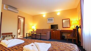 A hotel room with a bed, a desk, a chair, a sofa, and a television.