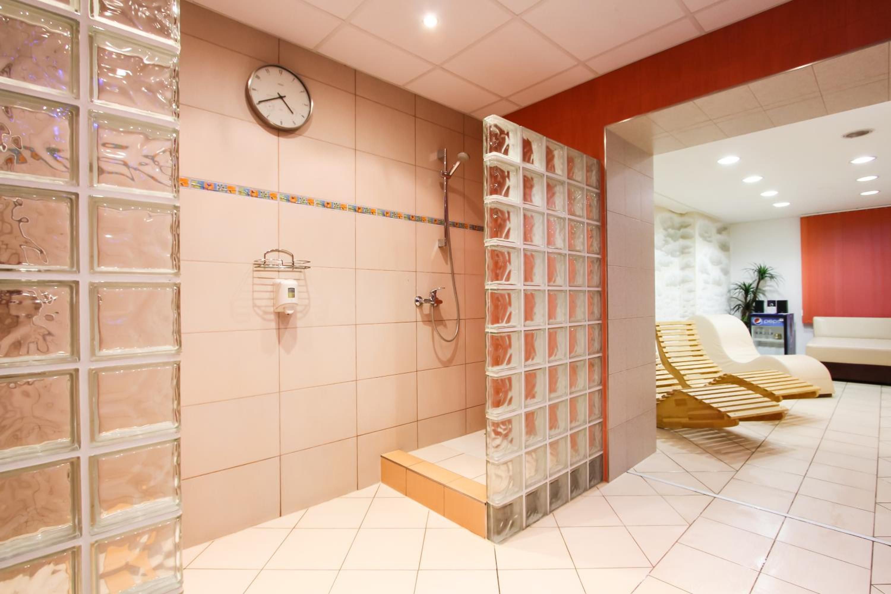 A modern spa with a glass shower enclosure, a clock, and a seating area with wooden loungers.