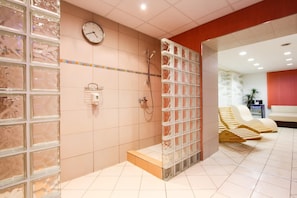A modern spa with a glass shower enclosure, a clock, and a seating area with wooden loungers. - Hotel Prajer (Vodňany)
