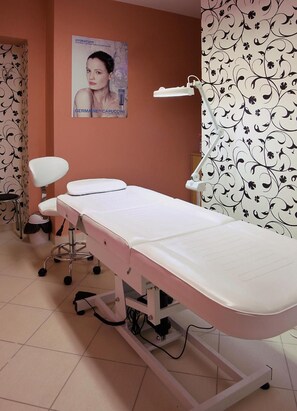 A medical examination table with a footrest, a white chair, and a poster on the wall.