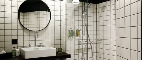 A modern bathroom with a black countertop, white sink, and a large mirror. There are two wall-mounted lights, a handheld showerhead, and a towel rack with towels.