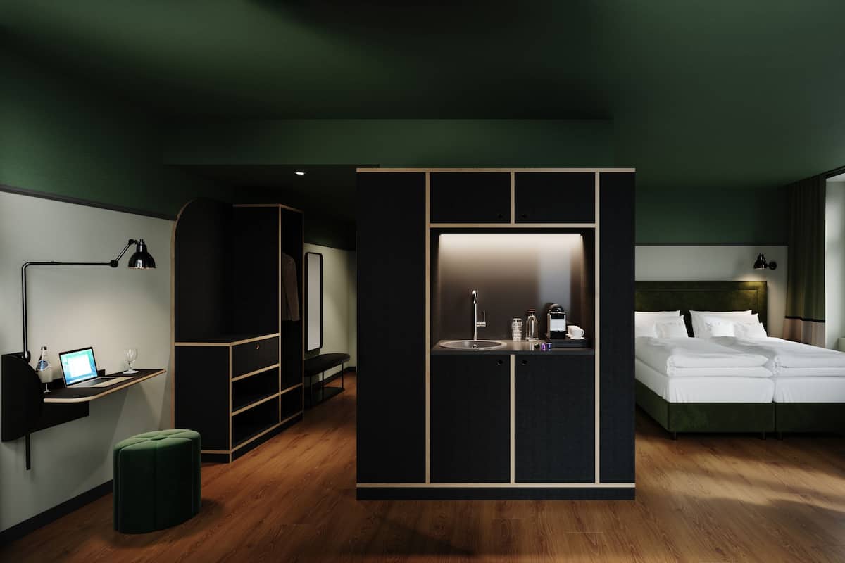 A modern hotel room with a wooden floor, a large bed, a desk with a laptop, a mirror, and a wardrobe.