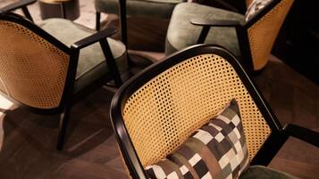 Una silla con respaldo de mimbre y un cojín a cuadros, parte de un comedor con mesas y sillas redondas.