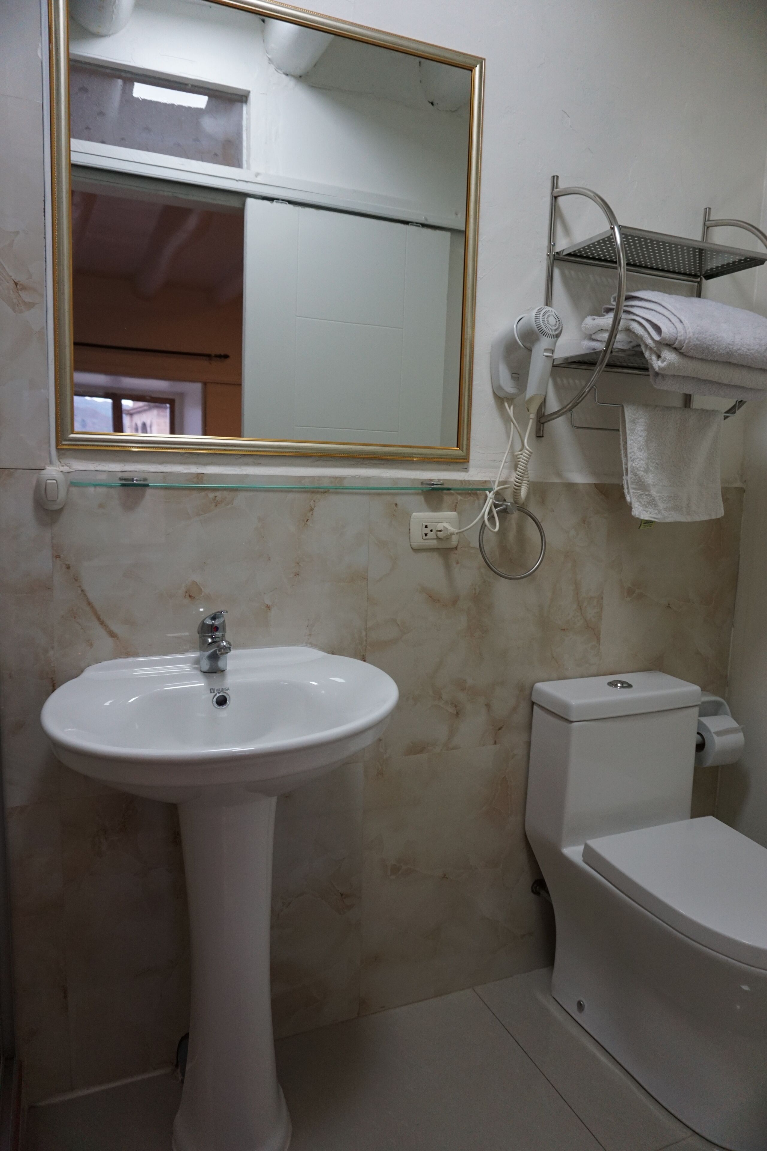 A bathroom with a pedestal sink, toilet, and a glass shelf with towels.