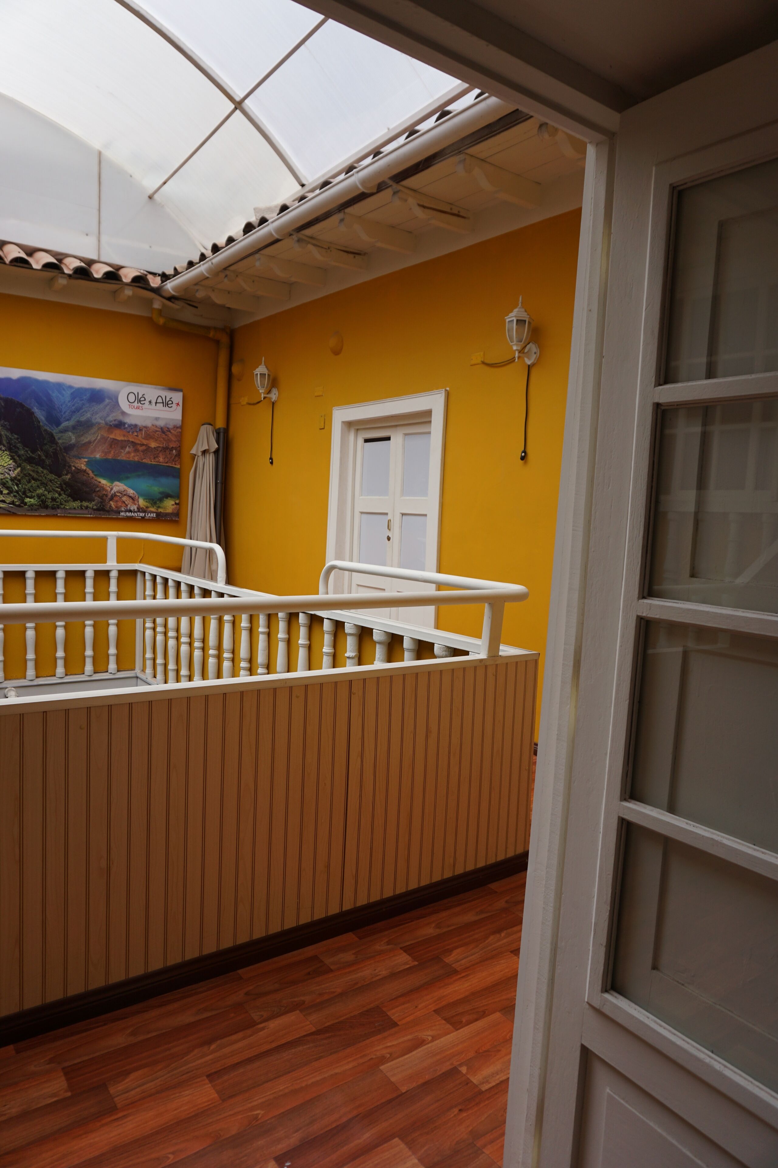 A room with a wooden floor, a white railing, a yellow wall, and a window with a view of a landscape.