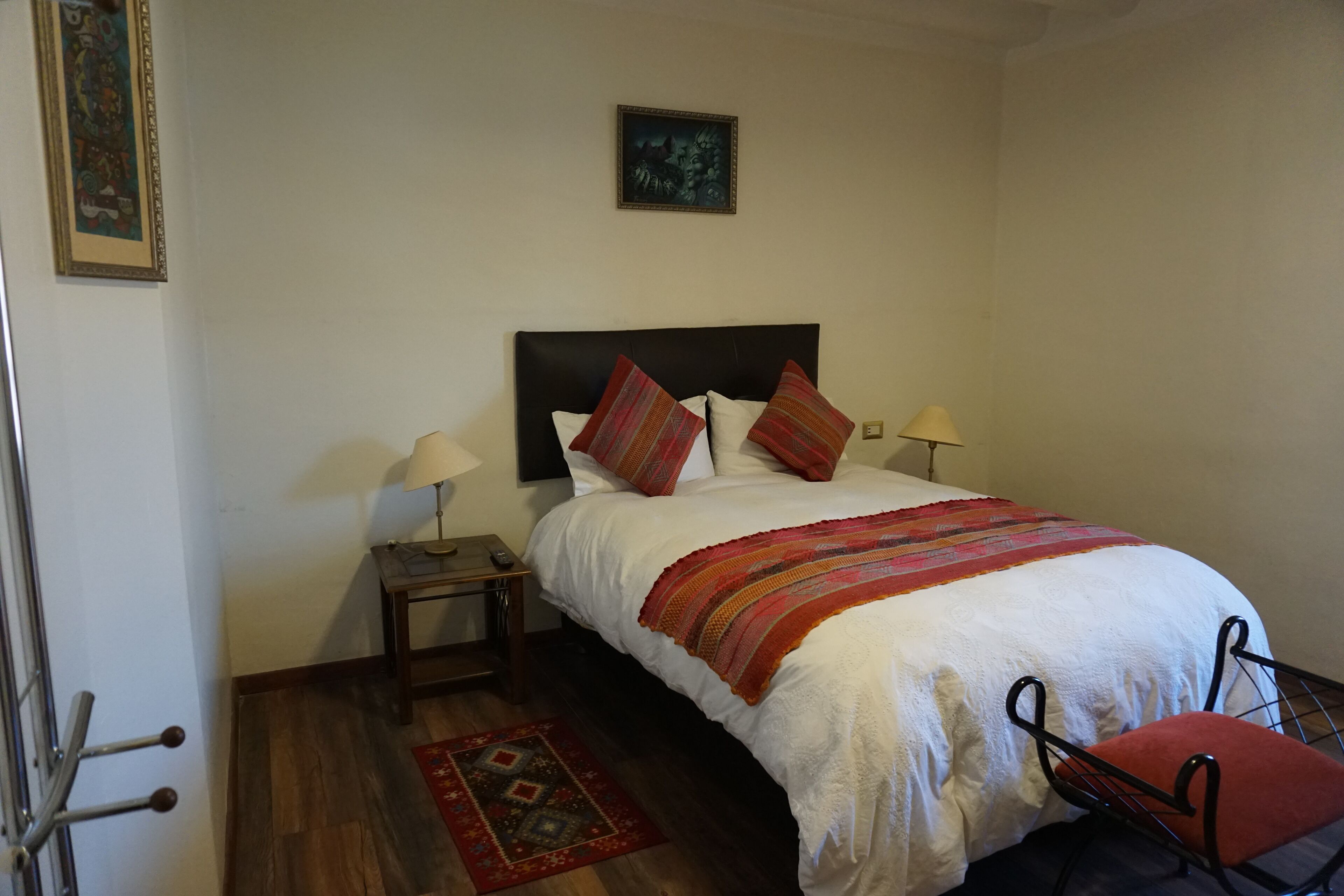 Una camera da letto ordinata con un letto, due comodini con lampade, una sedia, una porta e un piccolo tappeto.