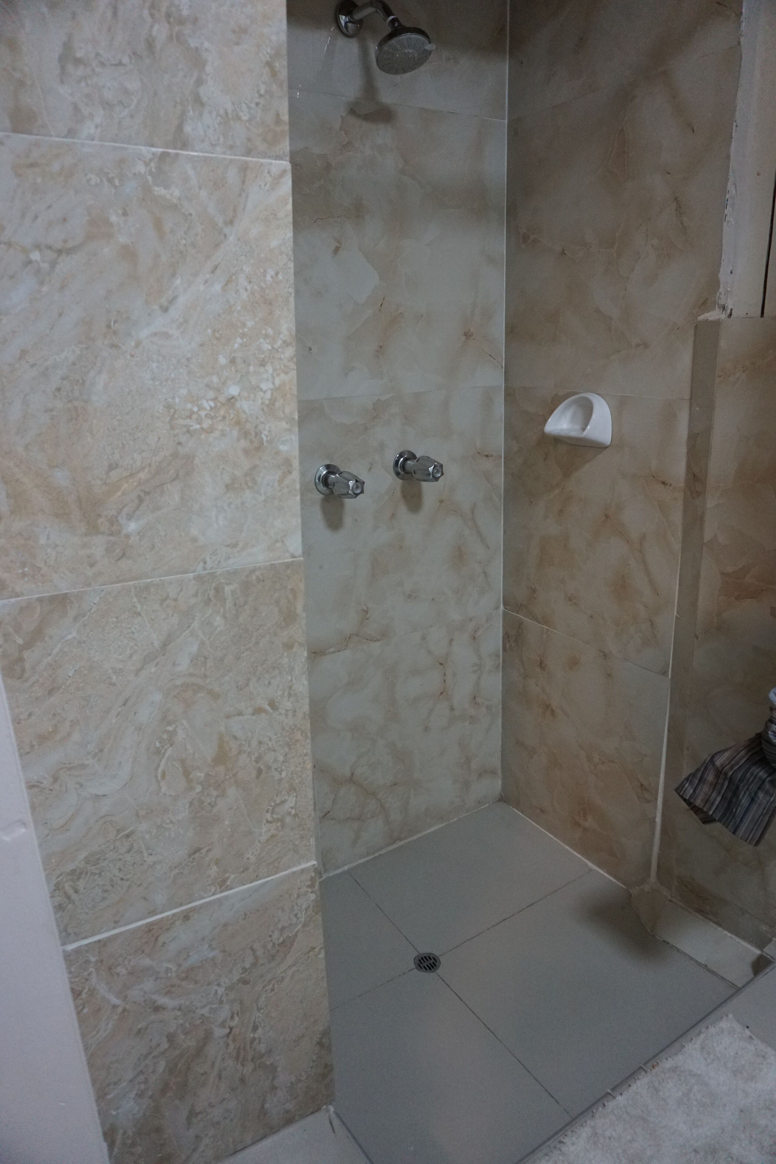 Un baño con azulejos de mármol color crema, ducha e inodoro.