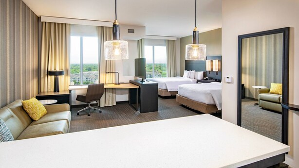 Una habitación de hotel con escritorio, dos camas, un sofá y un espejo grande.