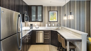Una cocina moderna con muebles oscuros, electrodomésticos de acero inoxidable, lavavajillas y una zona de bar con taburetes.