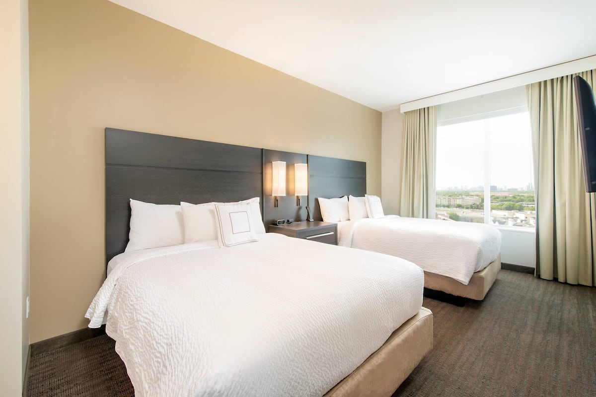 A hotel room with two beds, a large window with curtains, and a city view.