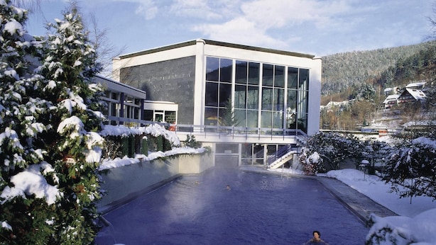 Un bâtiment moderne doté de grandes fenêtres, d’une piscine et entouré d’un paysage enneigé.