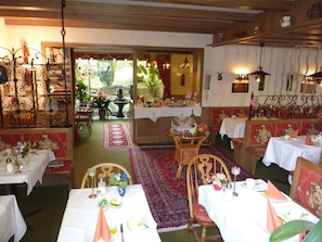A restaurant with multiple dining tables, chairs, and a variety of decorations including flowers and wall art. - Atina Hotel (Bad Wildbad)