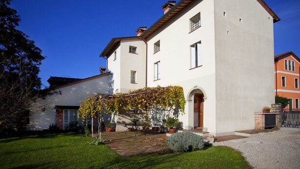 A two-story building with a white facade, a brick base, and a tiled roof. There is a small garden with a pathway leading to the entrance. - B&B Casa Fabbris (Sandrigo)