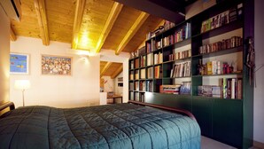 A bedroom with a large bed, wooden ceiling beams, a bookshelf, and a painting on the wall. - B&B Casa Fabbris (Sandrigo)