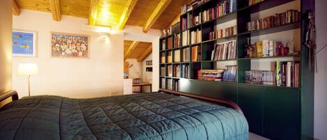 Una camera da letto con un letto grande, travi in legno a soffitto, una libreria e un quadro appeso al muro.