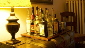 A dimly lit room with a vintage lamp, a collection of liquor bottles, a wooden chair, and a framed painting on the wall. - B&B Casa Fabbris (Sandrigo)