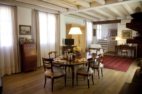 Un comedor con una mesa de madera, sillas, un televisor y un tapete rojo.