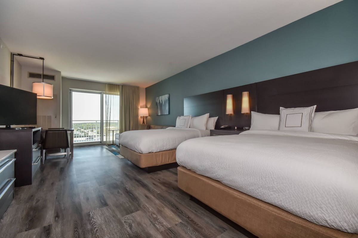 A hotel room with two beds, a TV, a desk, and a balcony with a view.