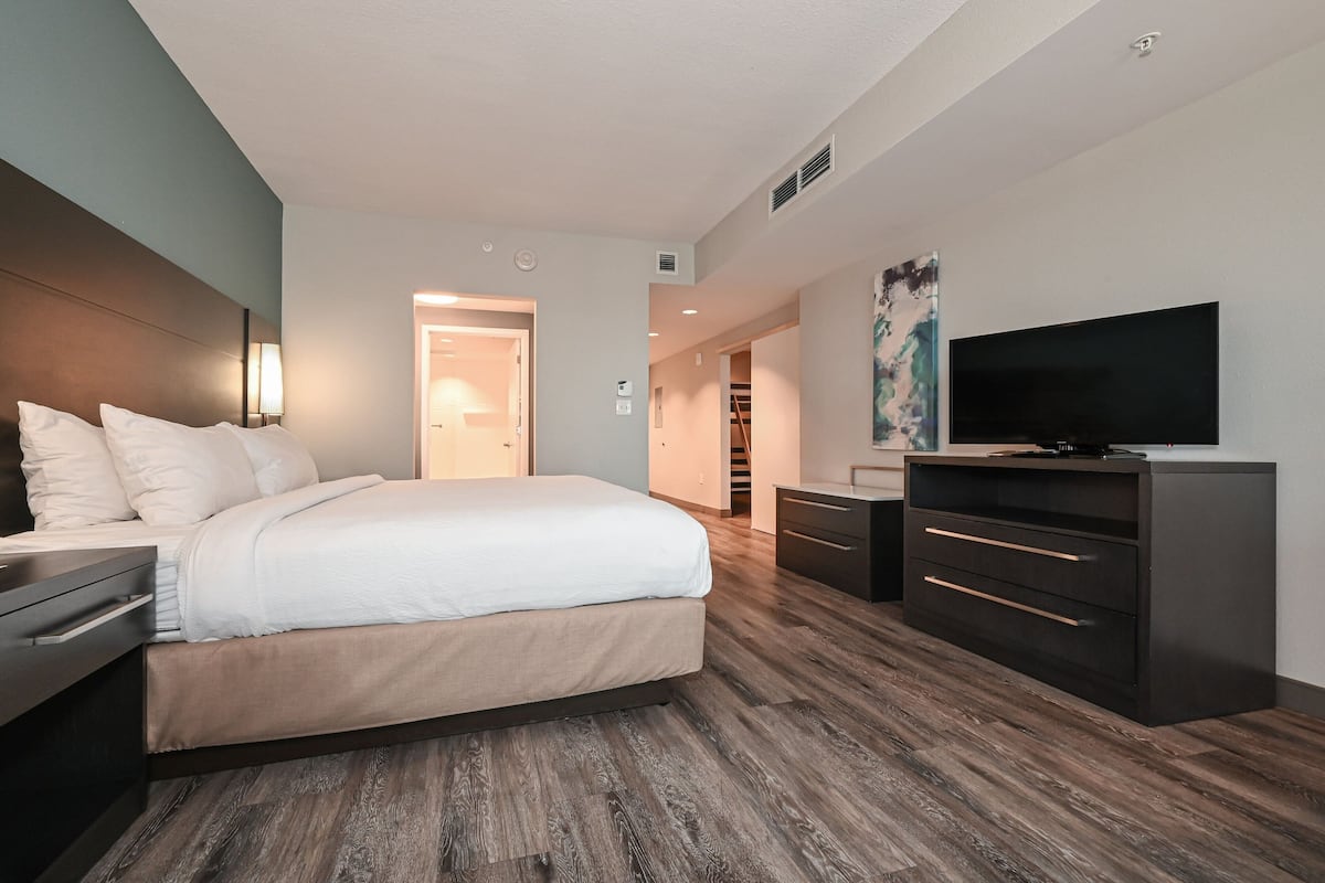 A modern hotel room with a large bed, a flat-screen TV, a desk, and a dresser.