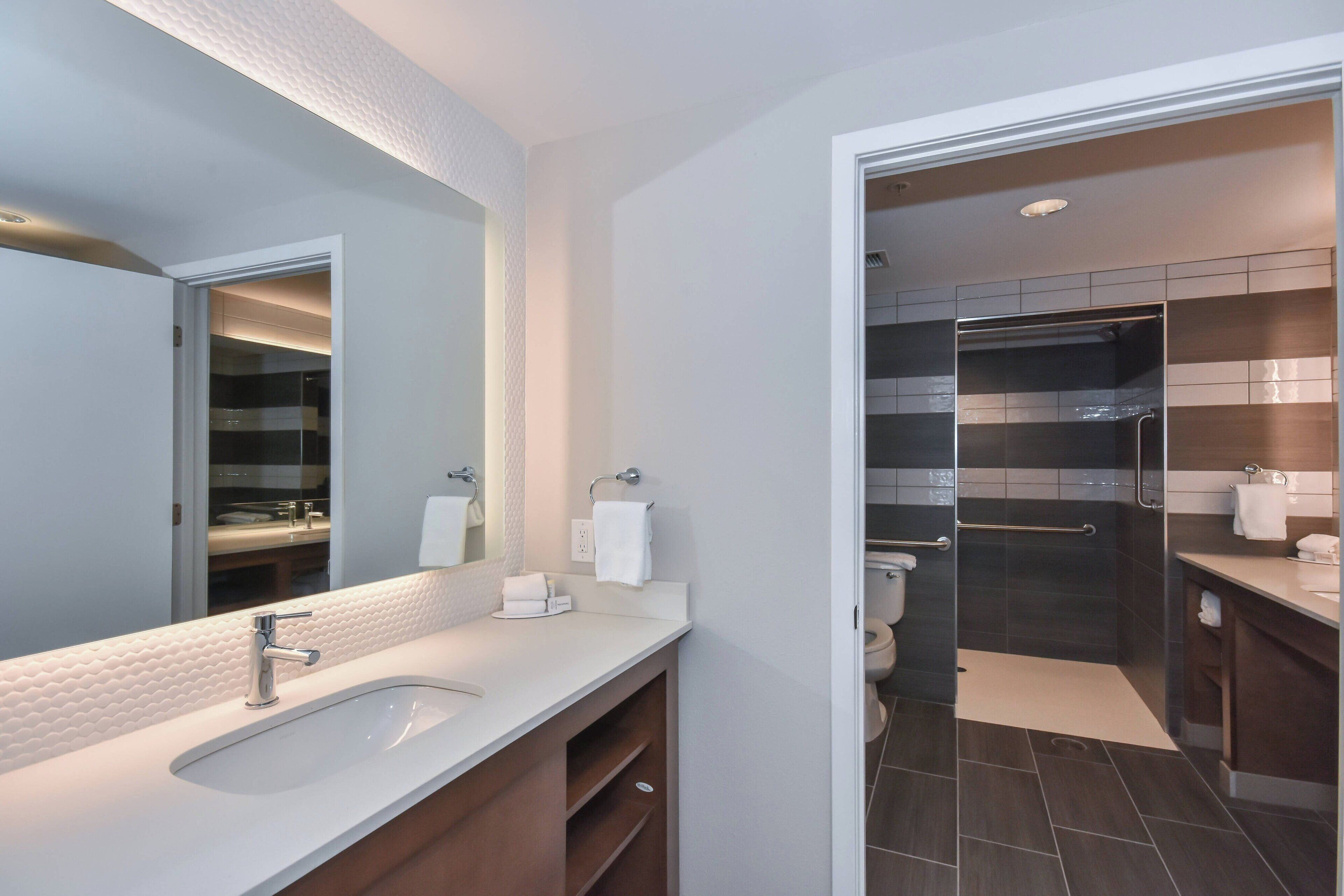 A modern bathroom with a white sink, a large mirror, and a shower area.