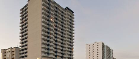 Un hotel moderno de gran altura con varios pisos, balcones y un área de entrada destacada con palmeras.