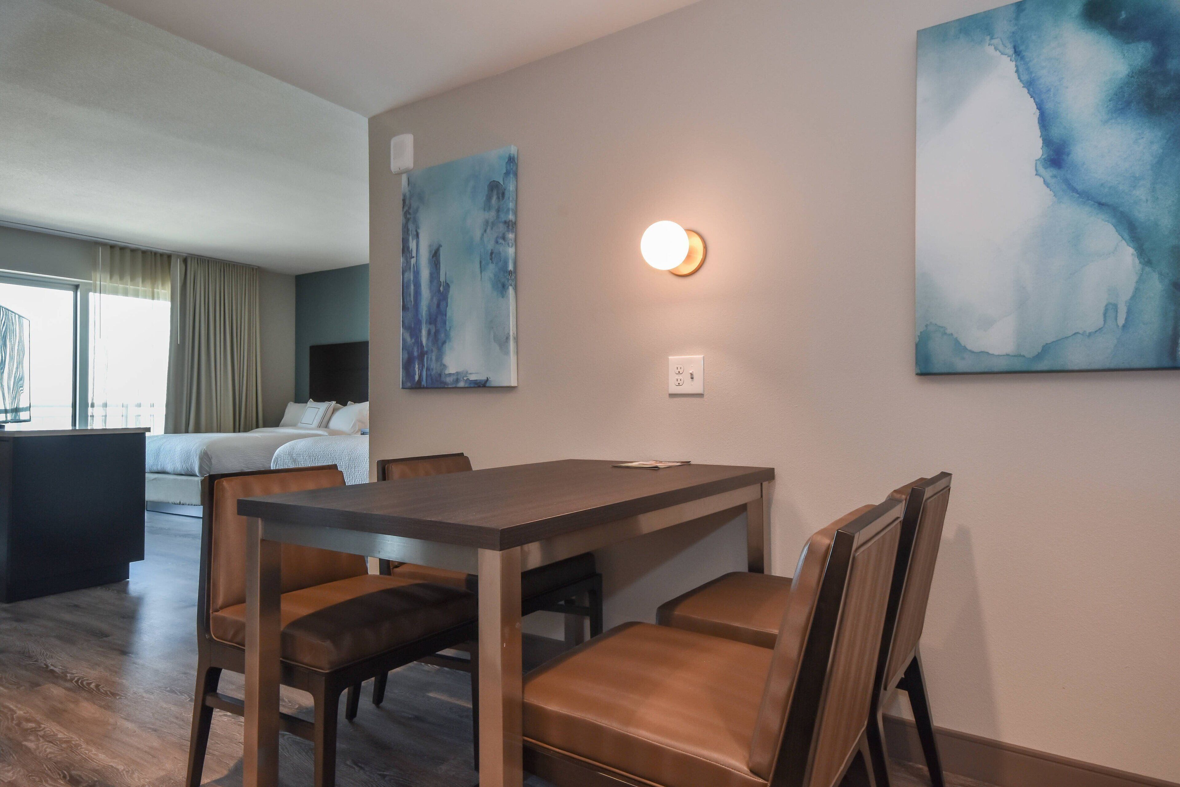 A modern hotel room with a dining area, a bed, and artwork on the walls.