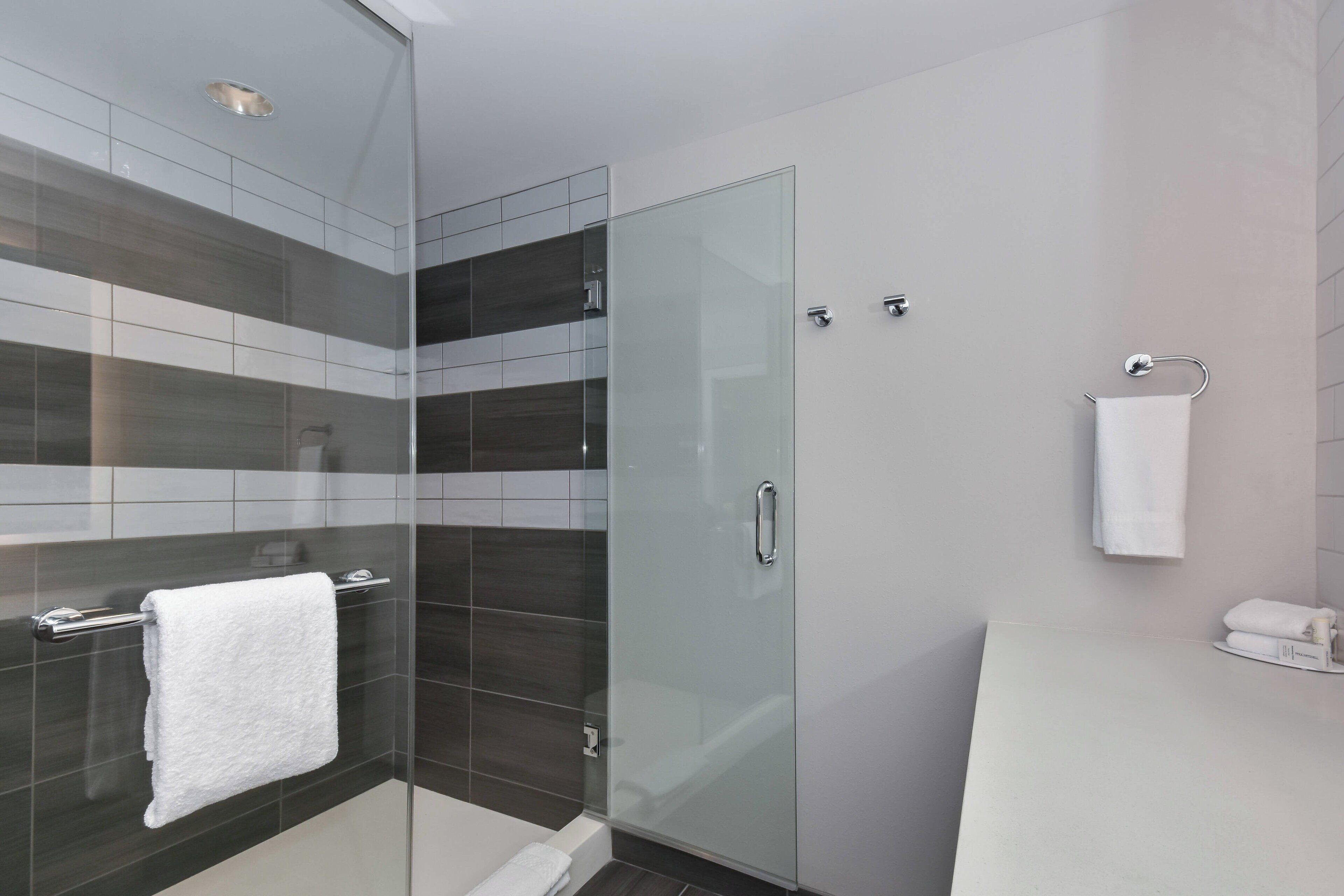 A modern bathroom with a glass shower enclosure, a white sink, and a towel rack.