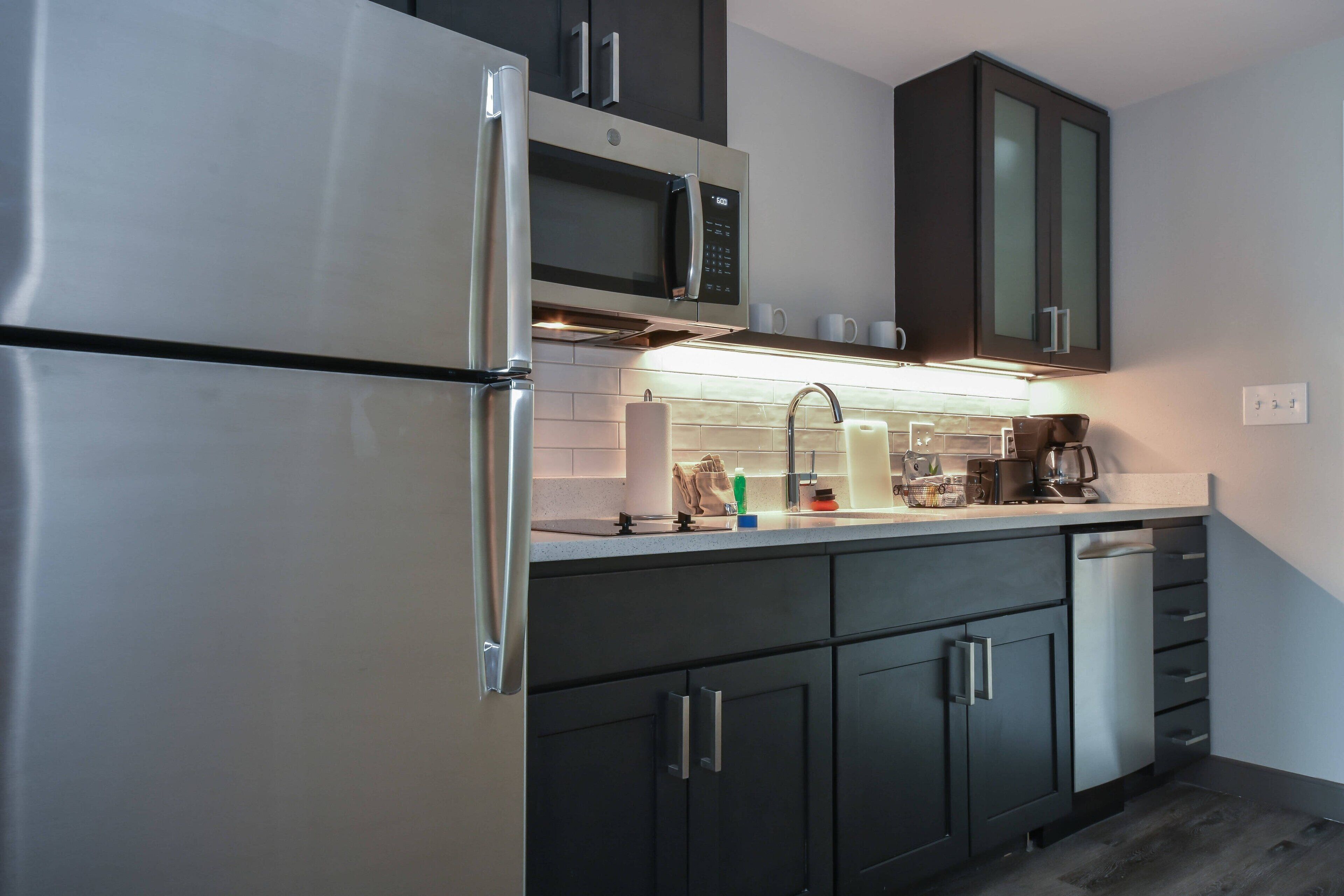 A modern kitchen with stainless steel appliances, dark cabinetry, and a built-in dishwasher.