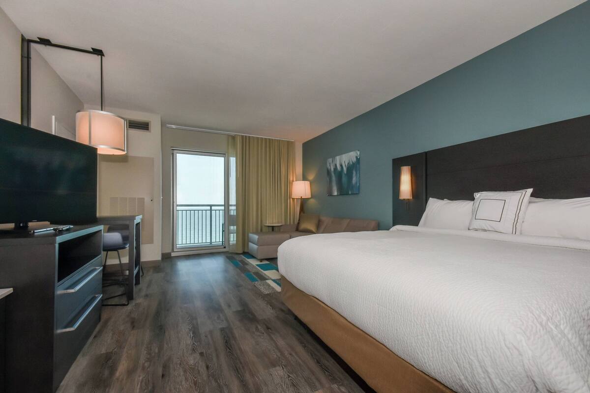 A hotel room with a large bed, a TV, a desk, and a balcony.