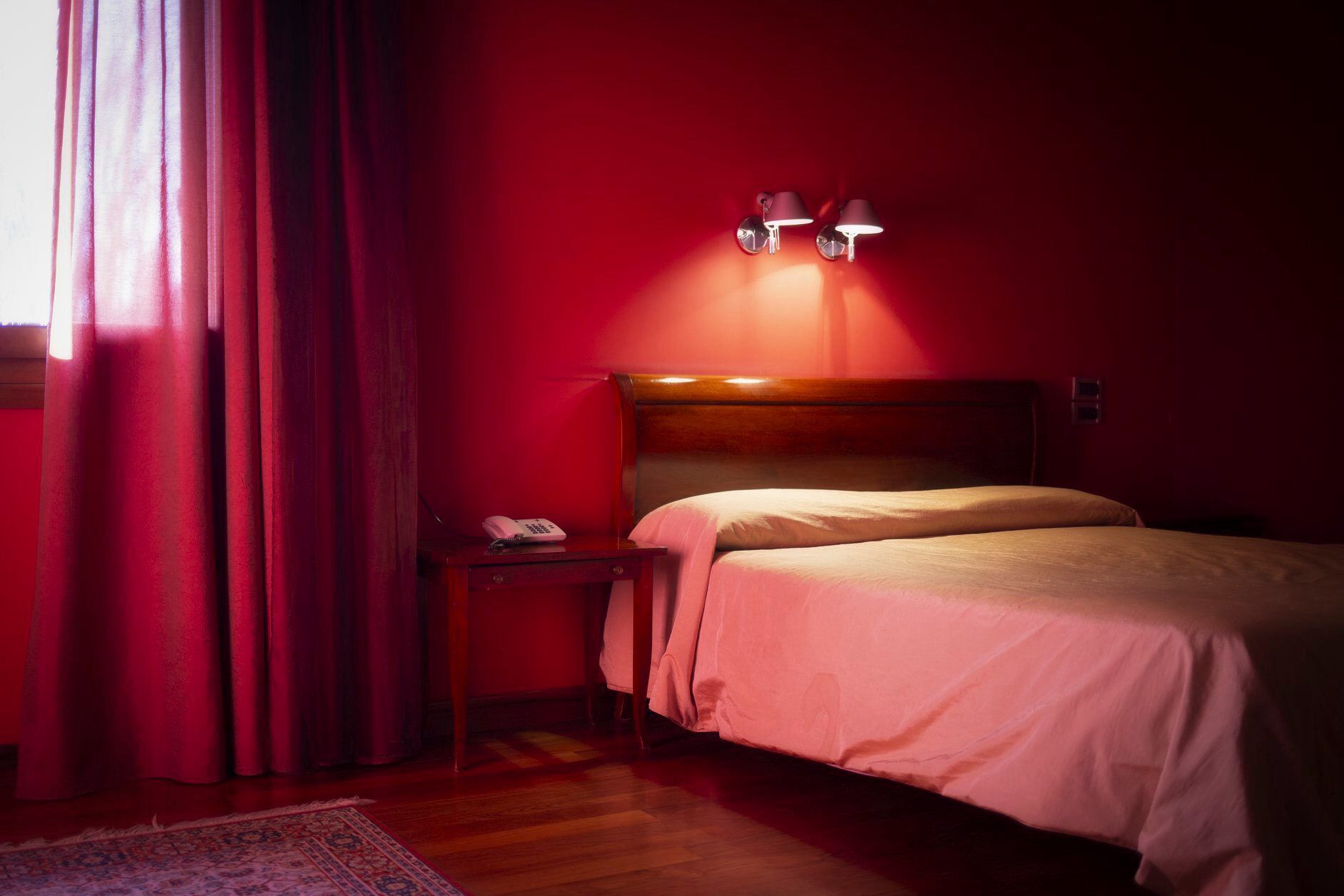 Une chambre d’hôtel avec une tête de lit en bois, une table de chevet avec un téléphone et un mur rouge.