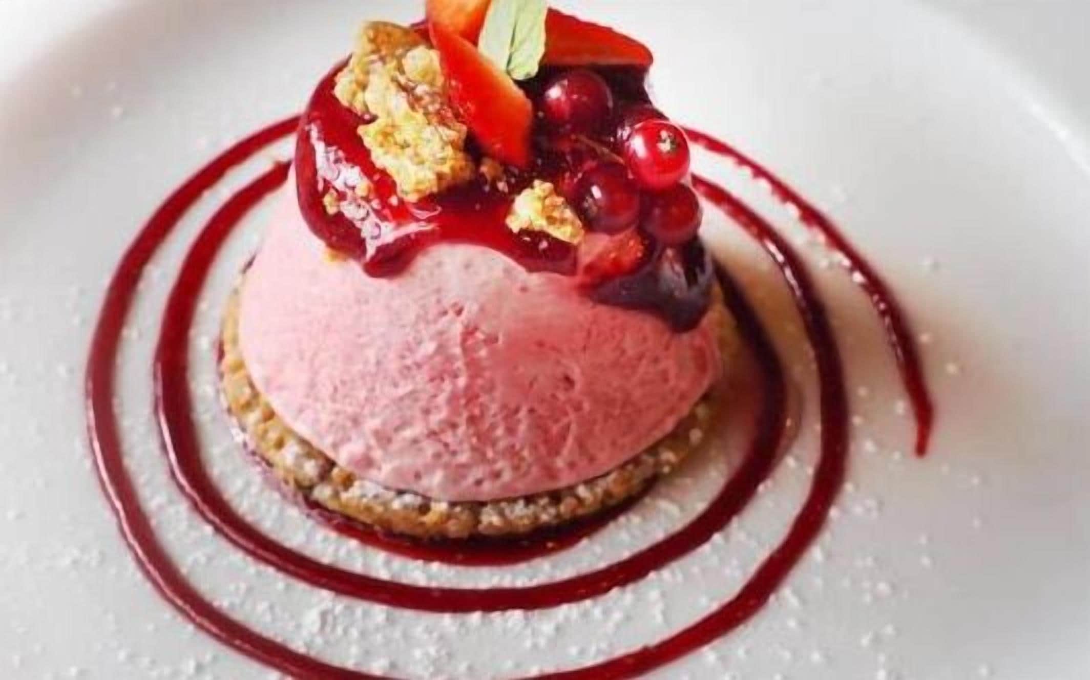 En efterrätt med bär som topping och en röd sås, serverad på en tallrik.