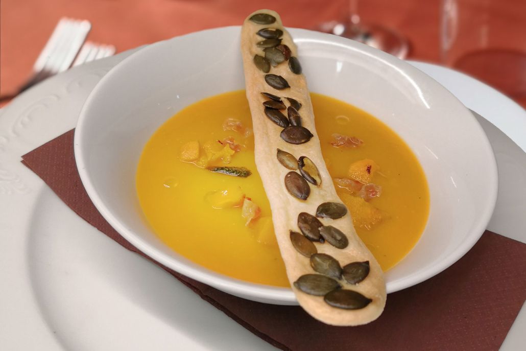 A bowl of soup with pumpkin seeds on a white plate.