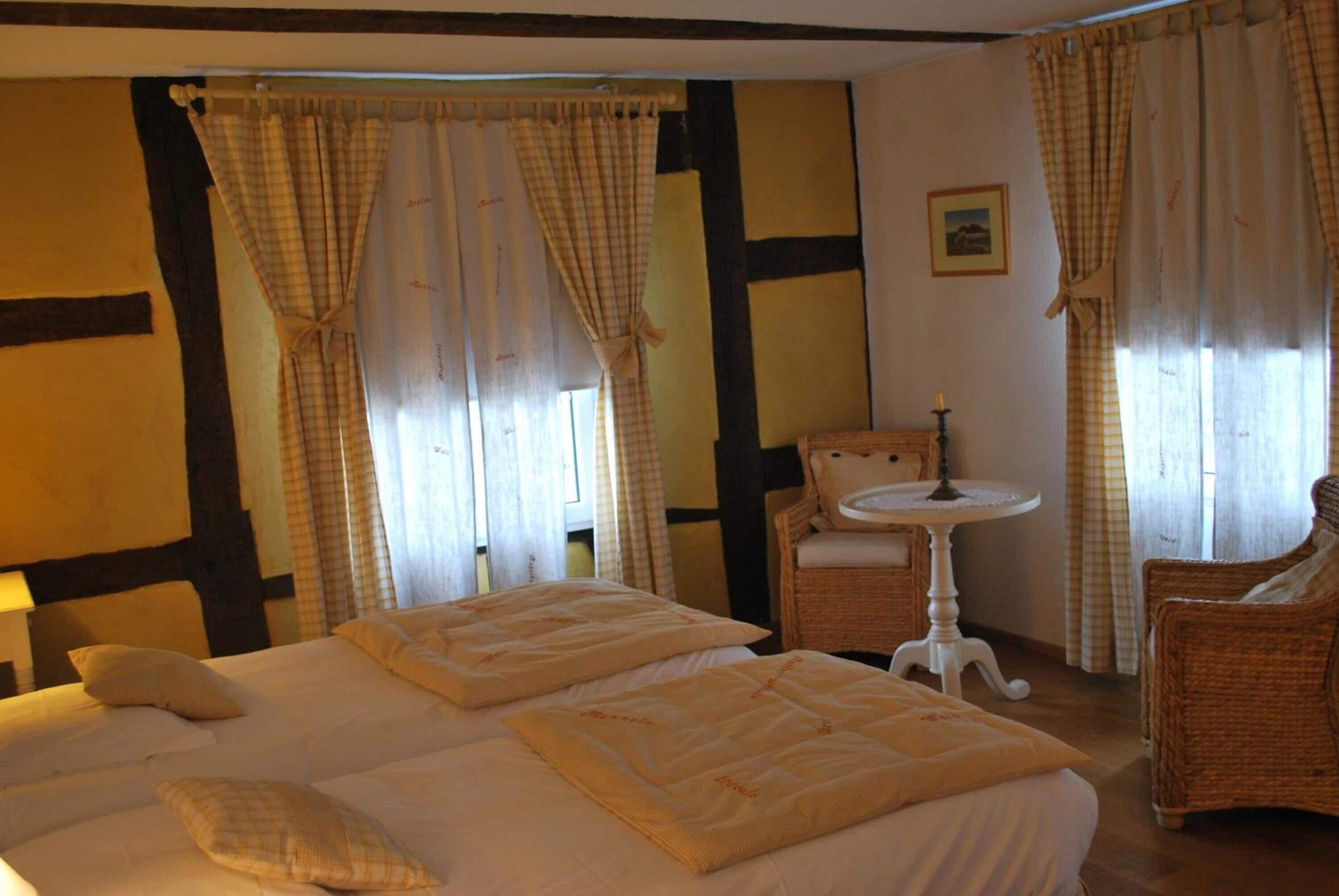 A hotel room with a large bed, two chairs, a small table, and curtains.