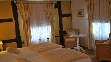 A hotel room with a large bed, two chairs, a small table, and curtains.