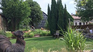 Un jardín con una estatua de gallo, césped y un edificio de fachada con entramado de madera.