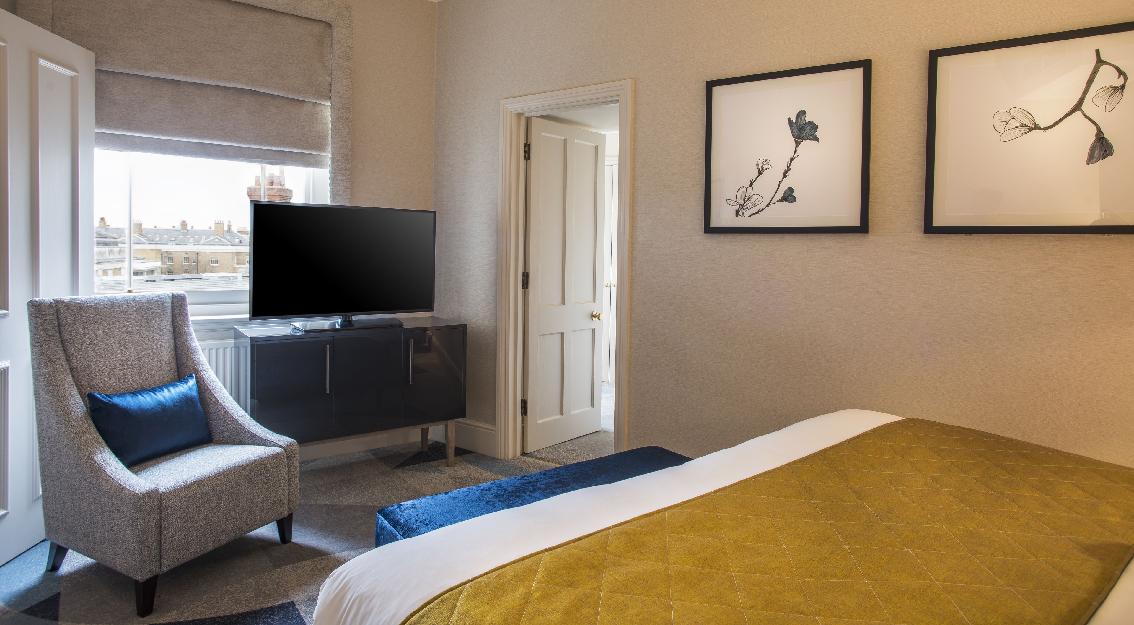 Ein Hotelzimmer mit einem Bett, einem Fernseher auf einer Kommode, einem Sessel und zwei gerahmten Bildern an der Wand.