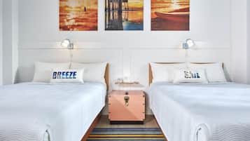 A hotel room with two beds, each with a pillow labeled "BREEZE" and "SALT." There are wall-mounted lamps, a wooden nightstand, and a suitcase.