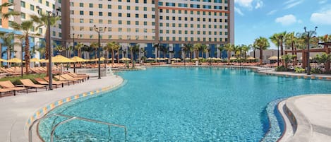 A hotel with a large pool, sun loungers, and palm trees.