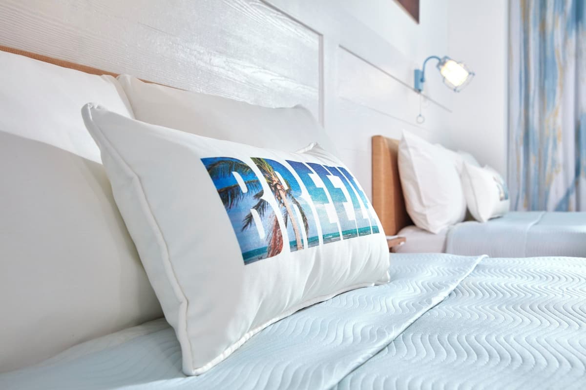 Ein ordentlich bezogenes Bett mit einem Kissen mit Strandmotiv, einem Holzkopfteil und einer Wandleuchte.