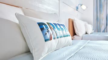 Un lit bien fait, avec un oreiller orné d’un motif représentant une plage tropicale, une tête de lit en bois et un luminaire fixé au mur.