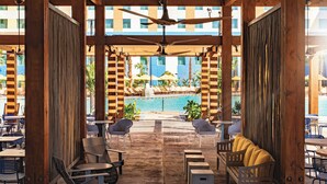 A covered outdoor seating area with wooden tables and chairs, a pool in the background, and a ceiling fan. - Universal's Endless Summer Resort - Dockside Inn and Suites (Orlando)