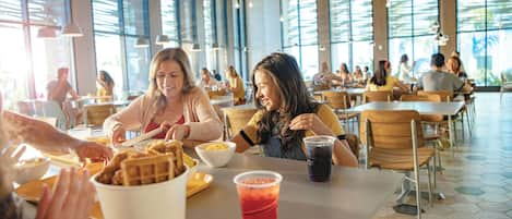 Un amplio comedor con techos altos y ventanas grandes, con mesas que exhiben diversos alimentos y bebidas.