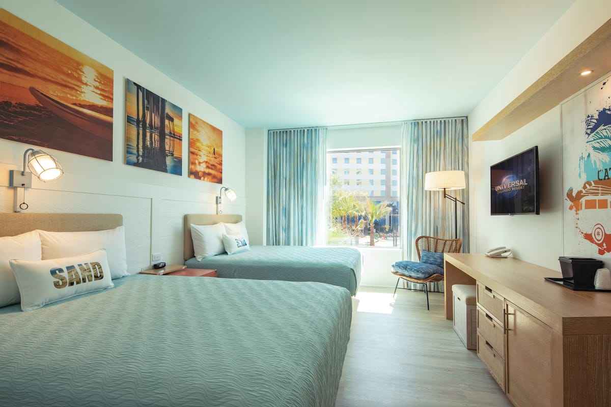 Ein Hotelzimmer mit zwei Betten, einem Schreibtisch, einem Stuhl und einem Fernseher.