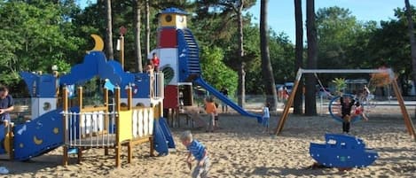 Un parque infantil con tobogán, estructuras para escalar y columpios sobre suelo arenoso.