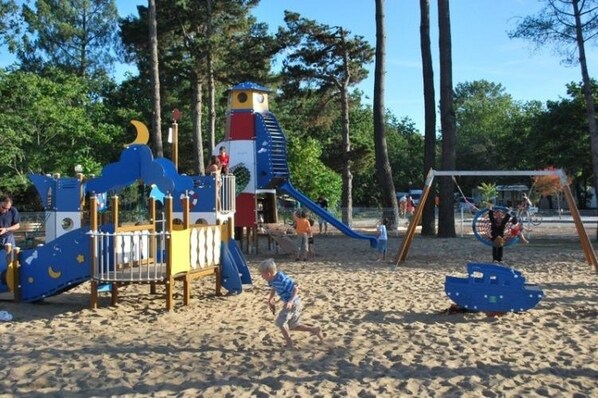 Ein Spielplatz mit Rutsche, Klettergerüsten und Schaukeln auf Sandboden.